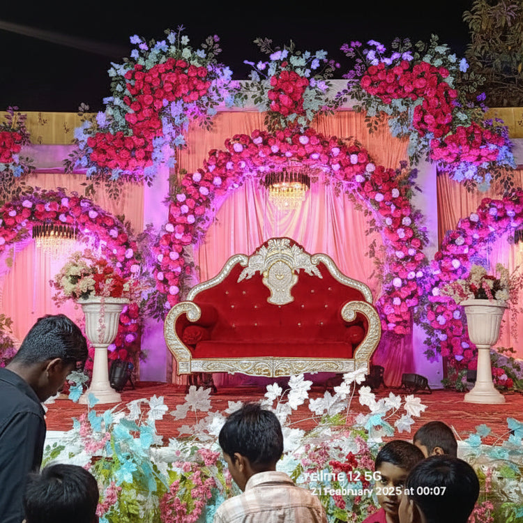 Decorated stage with floral arrangements and a red chair, likely for an event or celebration.